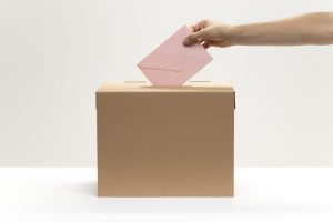 une-main-met-une-enveloppe-rose-dans-la-boite-de-vote une-main-met-une-enveloppe-rose-dans-la-boite-de-vote